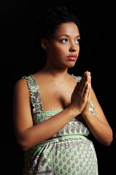 Young beautiful afro american pregnant woman praying against black background