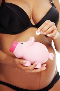 Young beautiful pregnant woman holding a pink piggybank in front of her belly, over a white background.