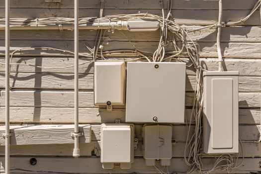 Messy cables and electrical boxes in a wooden beige painted wall facade