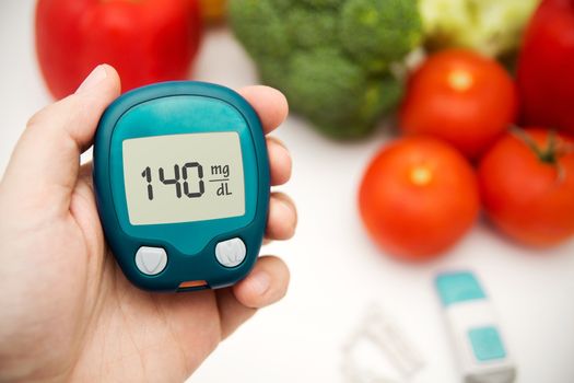 Hand holding meter. Diabetes doing glucose level test. Vegetables in background