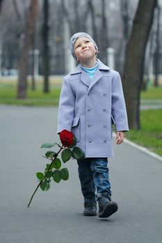 Little romantic boy with rose walking in the park