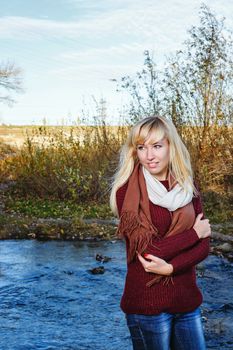 Attractive young blonde girl in sweater on alone bank of river