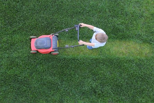 Little boy cuts a lawn using lawn-mower