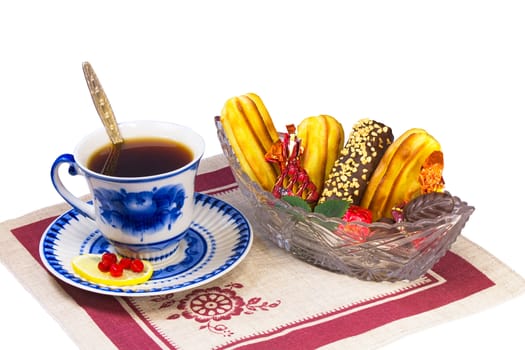 Cup of tea, candies and cakes in the basket are located on a napkin from flax. Presented on a white background.