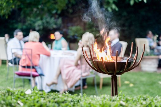 Group of people enjoying a garden party. In the foreground a Firebowl