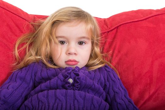 Cute solemn beautiful young girl staring at the camera with a calm expression as she relaxes on a comfortable red cushion in her colourful purple sweater