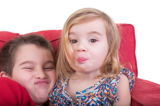 Young brother and sister pulling funny faces holding their breath and screwing up their noses as they sit together playing on a red couch