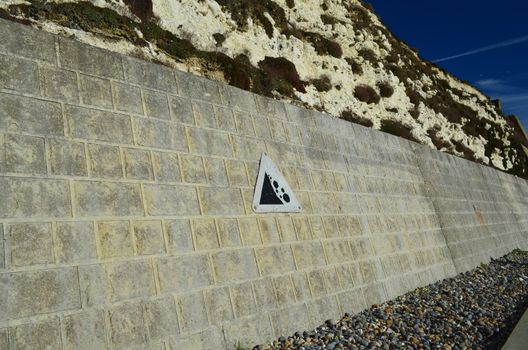 Along a stretch of cliff a warning sign informs path users of possible rock falls from cliff above.