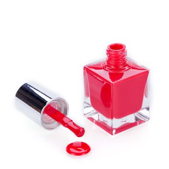 Modern stylish red nail varnish or lacquer displayed as an open glass bottle with the applicator alongside dripping onto a clean white surface with copyspace