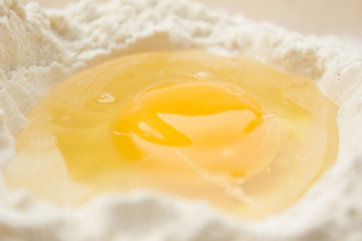 Flour on a wooden cutting board with a egg in the middle of it.