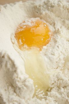 Flour on a wooden cutting board with a egg in the middle of it.