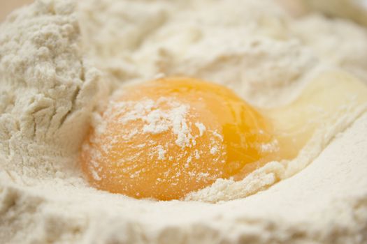 Flour on a wooden cutting board with a egg in the middle of it.