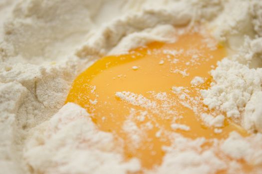 Flour on a wooden cutting board with a egg in the middle of it.