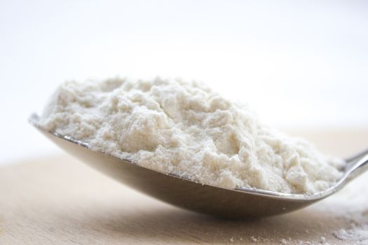 Metal spoon full with flour on a wooden cutting board.