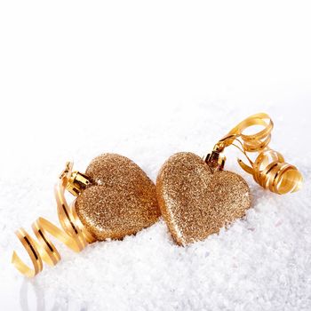 Two gold hearts on snow. Two hearts with gold tapes on snow. Christmas-tree decorations in the form of hearts. Valentine's Day. February 14. Winter holiday.