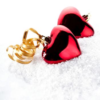 Two red hearts on snow. Two hearts with gold tapes on snow. Christmas-tree decorations in the form of hearts. Valentine's Day. February 14. Winter holiday.