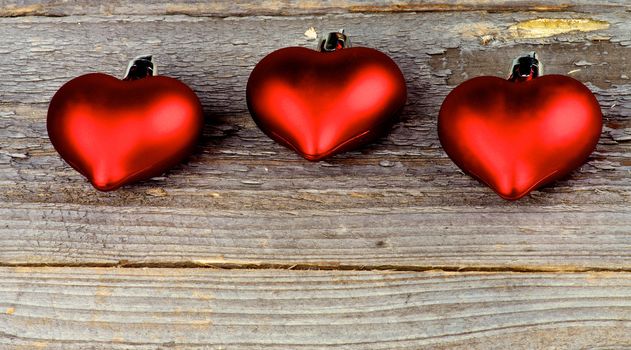 Three Red Plastic Hearts In a Row closeup on Rustic Wood background