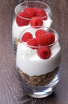  Delicious Dessert with Fresh Ripe Raspberries, Muesli and Dairy Cream in Two Glasses In a Row closeup on Wooden background