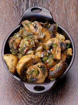 Delicious Champignon Mushrooms Stew with Onion and Greens in Black Cast-iron Stew Pot on Wooden background. Top View