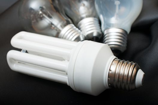 Energy Saving Bulb and Three Aged Burnt Tungsten Bulbs on Black Background