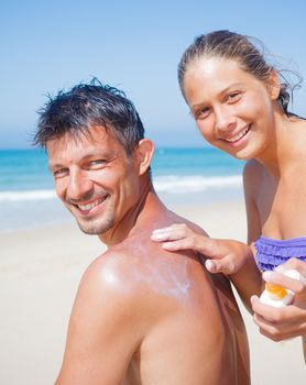 Adorable girl at tropical beach applying sunblock cream on a father's back.