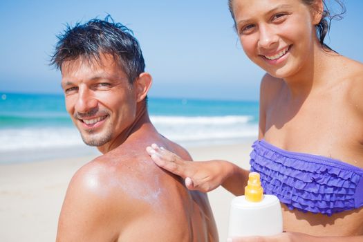 Adorable girl at tropical beach applying sunblock cream on a father's back.