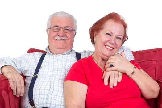 Good natured senior couple relaxing together in a close embrace looking at the camera with charming friendly smiles