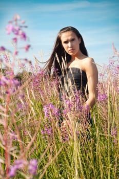 Outdoor shot of beautiful brunette woman with long hair standing in grass and flowers