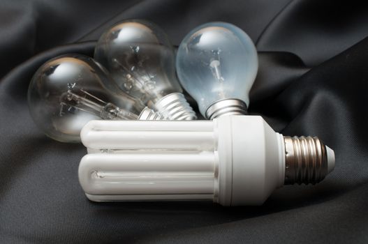 Energy Saving Bulb and Three Aged Burnt Tungsten Bulbs on Black Background