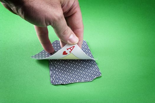 Hand discovering a lcard of poker as hearts on a green background
