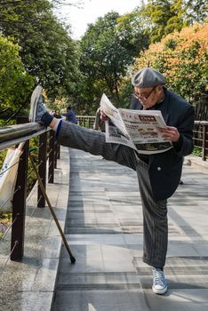 Shanghai, China - April 7, 2013: one old man exercising stretching splits and reading newspaper in gucheng park at the city of Shanghai in China on april 7th, 2013