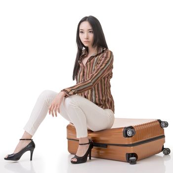 Asian woman thinking and sitting on a luggage, full length portrait isolated on white background.