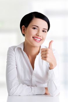 Young woman at the desk gesturing OK , isolated on white