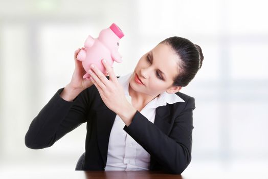 Happy business woman with her savings in piggy bank at the desk, isolated