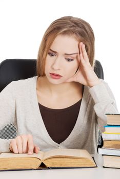 Beautiful casual woman student worried, scared is sitting by a desk and stack of books. Isolated on white.