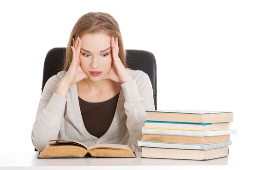 Beautiful casual woman student worried, scared is sitting by a desk and stack of books. Isolated on white.