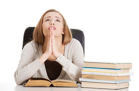 Beautiful student woman sitting and praying with stack of books. Isolated on white.