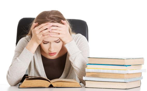 Beautiful casual woman student worried, scared is sitting by a desk and stack of books. Isolated on white.