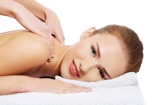 Young beautiful caucasian woman lying on a massage table and is being massaged. Isolated on white.