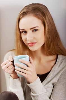 Beautiful casual caucasian woman sitting with hot drink of coffee or tea. Indoor background.