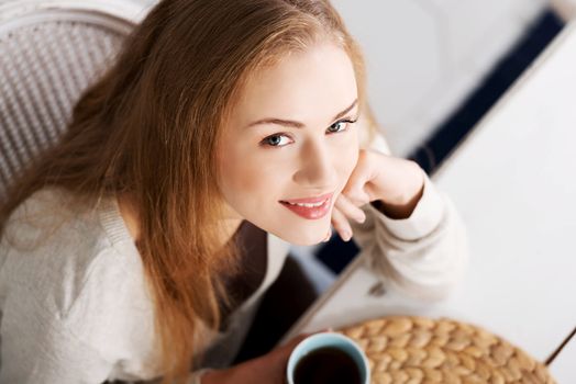 Beautiful caucasian woman sitting by a table with black coffee. Up front view.