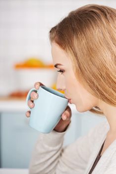 Beautiful caucasian woman is drinking hot drink, profile view. Indoor background.