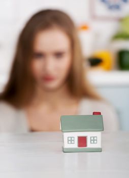 Beautiful caucasian woman and small house model. Focus on house. Indoor background.