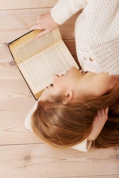 Young beautiful woman lying on the wooden floor with books.