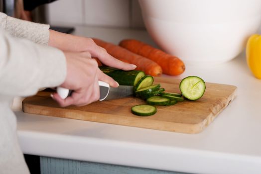 Beautiful woman in cutting cucumber on kitchen board. Indoor background.