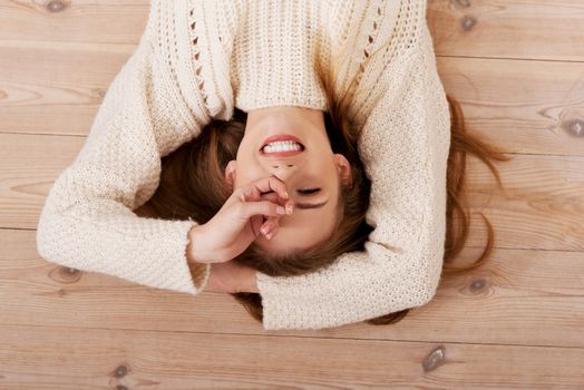 Picture of a careless young caucasian woman on the wooden floor wearing bright sweater.