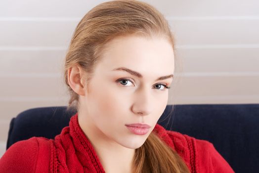 Beautiful caucasian woman sitting ona couch and wearing red pullover. Indoor background.