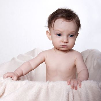 Little baby boy sitting naked on a blanket, in a box, on a white background