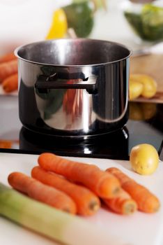 Kitchen pot on an gas plate and lying vegetables on kitchen board next to it.