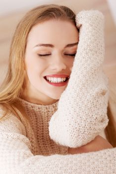 Beautiful caucasian woman is sitting on wooden floor and wearing bright sweater.